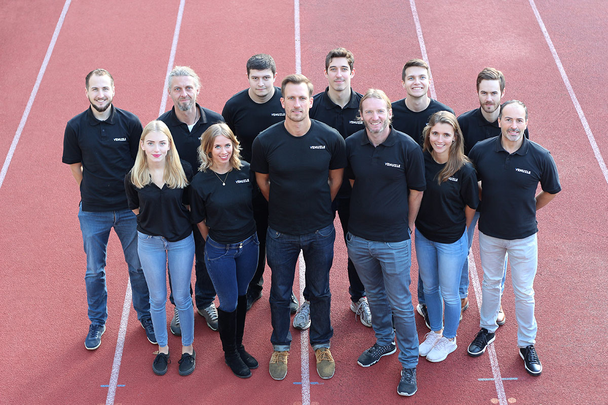 Venuzle Teamfoto mit 12 Personen mit schwarzem Venuzle Team Shirt, die auf einer roten Laufbahn in Graz stehen